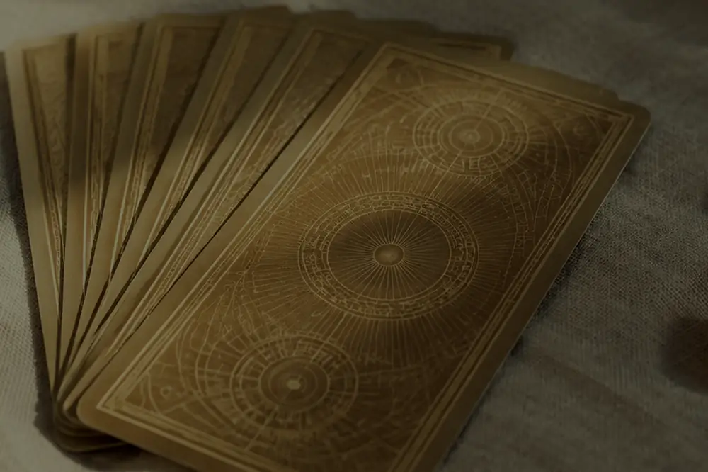 Detalhe do verso ornamentado das cartas douradas usadas na leitura, sobre linho cru