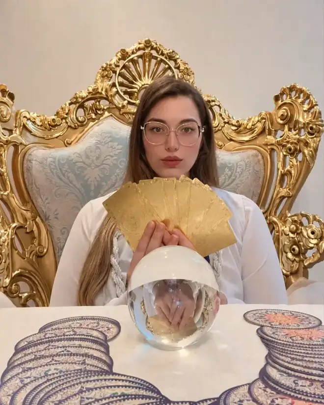 Taróloga Valentina com um leque de cartas douradas sobre a bola de cristal na mesa de atendimento