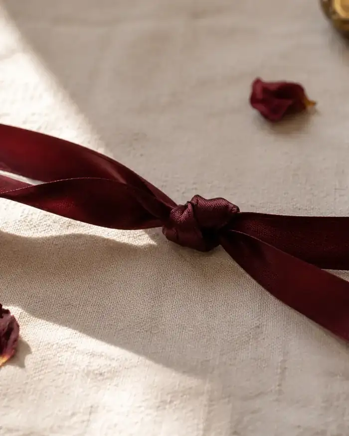 Duas fitas de seda vinho entrelaçadas em um nó, com pétalas de rosa secas ao redor