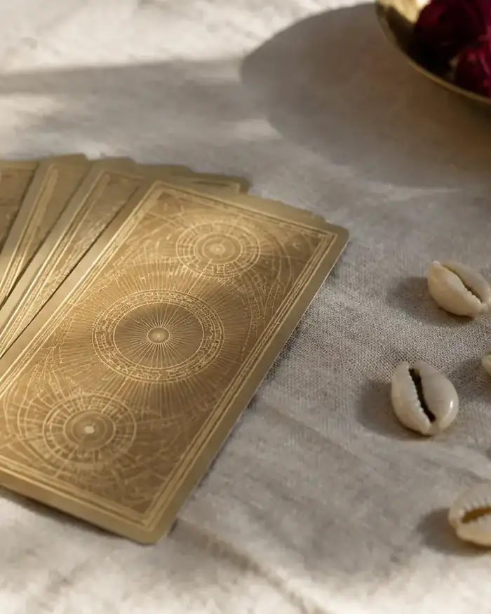 Leque de cartas douradas de tarot e conchas de búzios sobre tecido de linho cru
